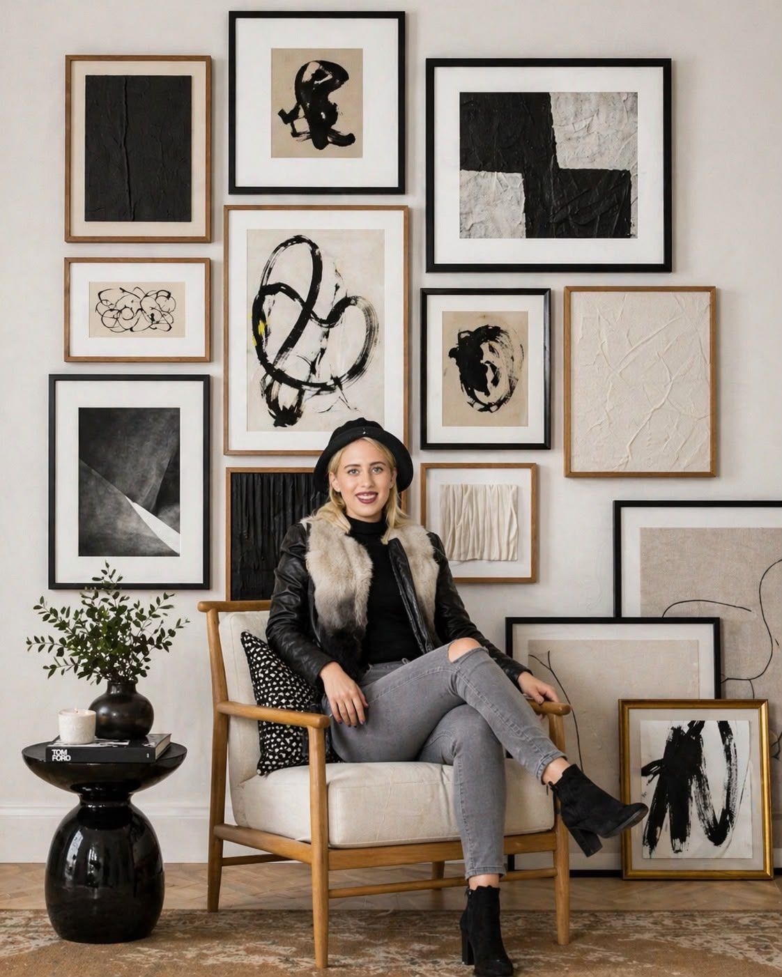 gallery wall of framed monochrome abstract prints in mixed timber and black frames above a wooden armchair