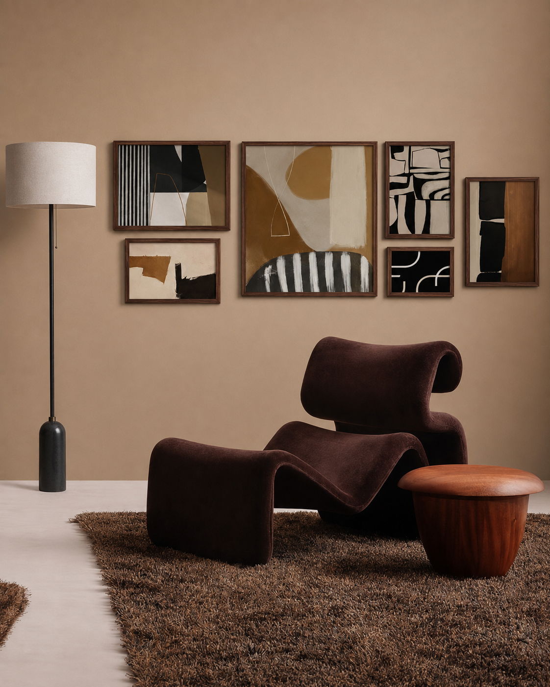 Gallery wall of six framed abstract prints in dark wood frames on a warm tan wall, above a brown velvet lounge chair and ottoman